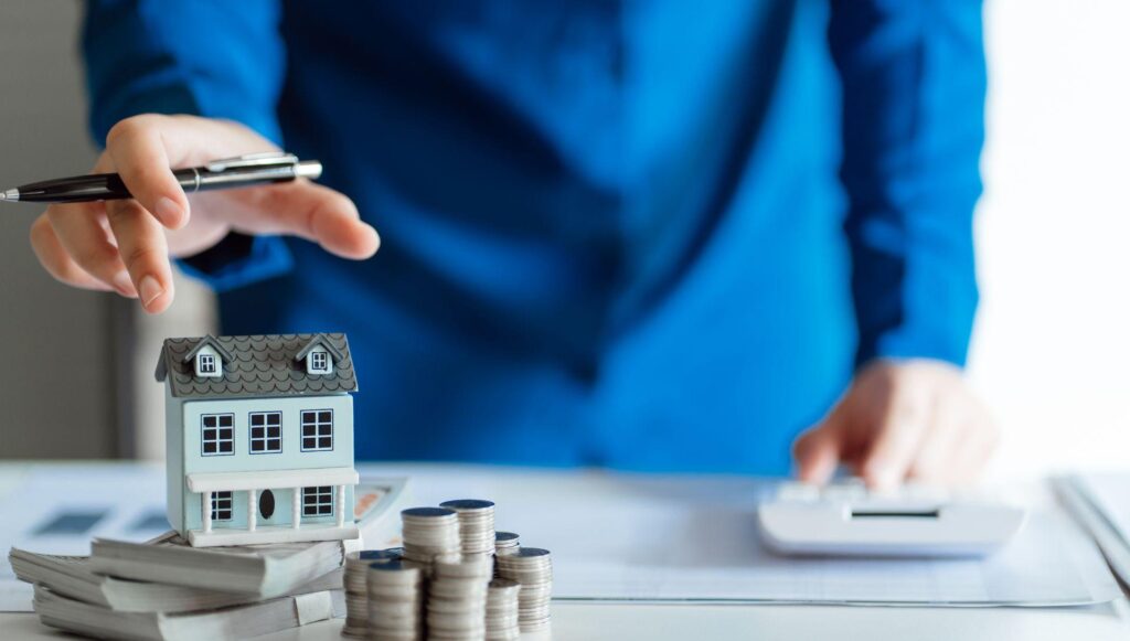 a person reaching for a home sitting on a pile of money.